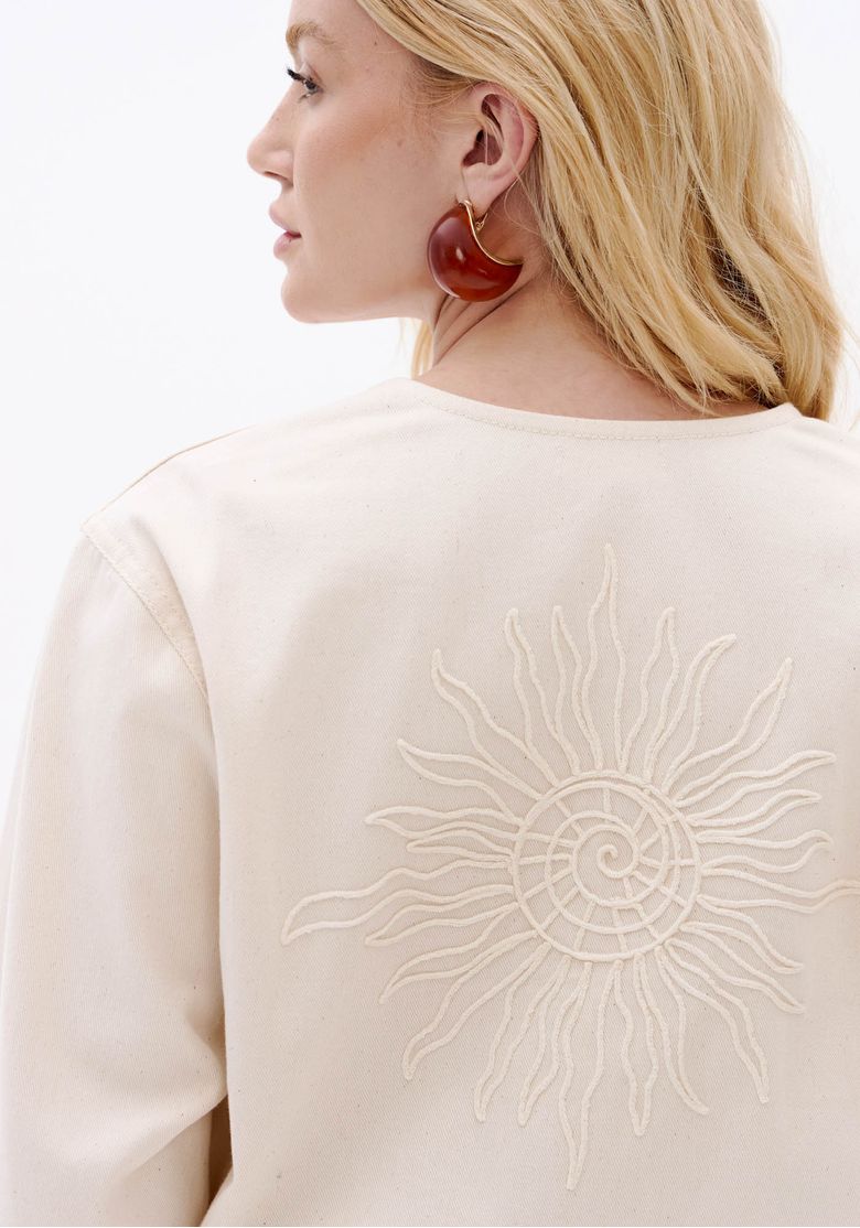 Close nas costas da jaqueta feminina off white com bordado localizado em desenho de sol e acabamento em sarja