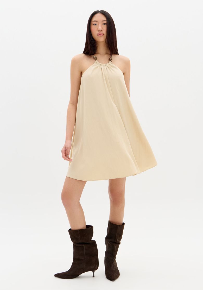 Modelo-em-pose-frontal-com-vestido-gode-bege-em-movimento-evidenciando-leveza-do-tecido-e-barra-reta-acima-do-joelho---vestido-fluido-bege