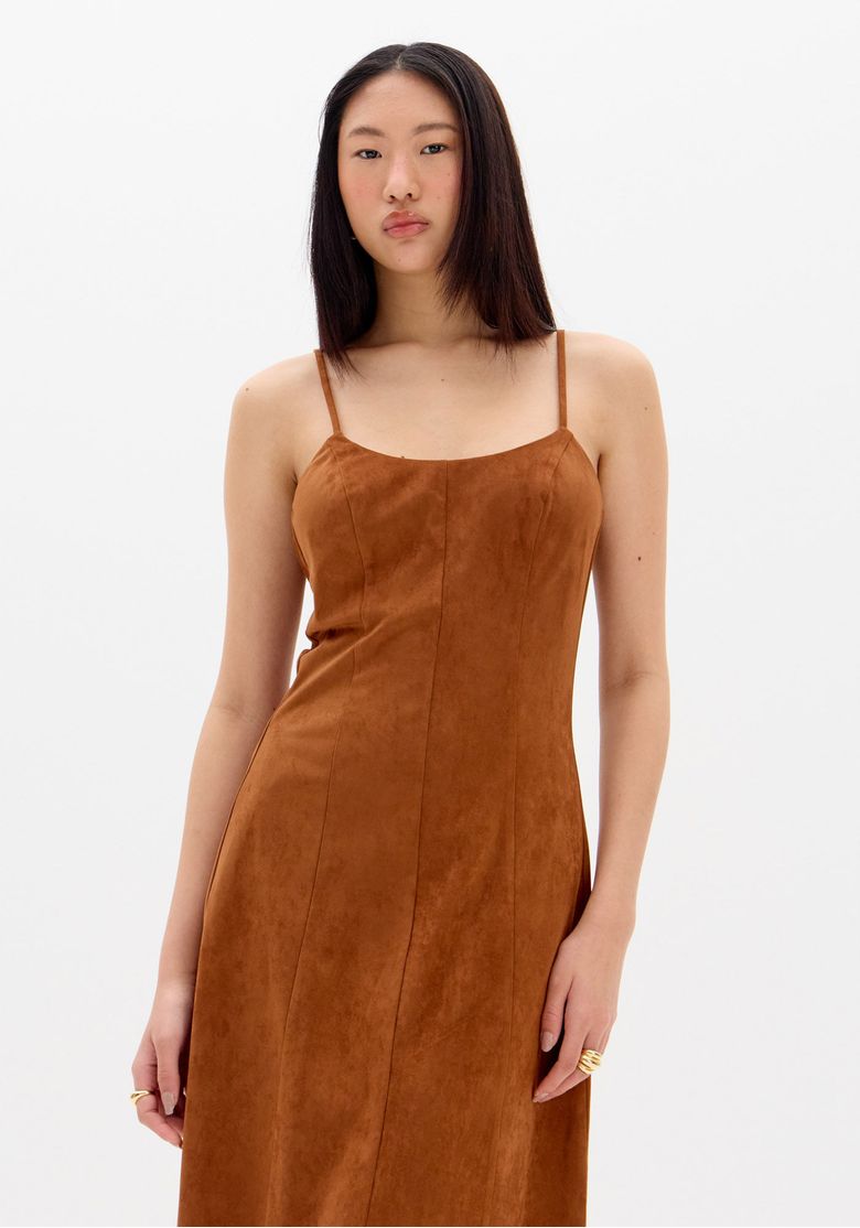 Modelo-em-cenario-com-painel-de-madeira-usando-vestido-super-midi-marrom-em-camurca-vista-frontal-corpo-inteiro-com-styling-dia-a-noite