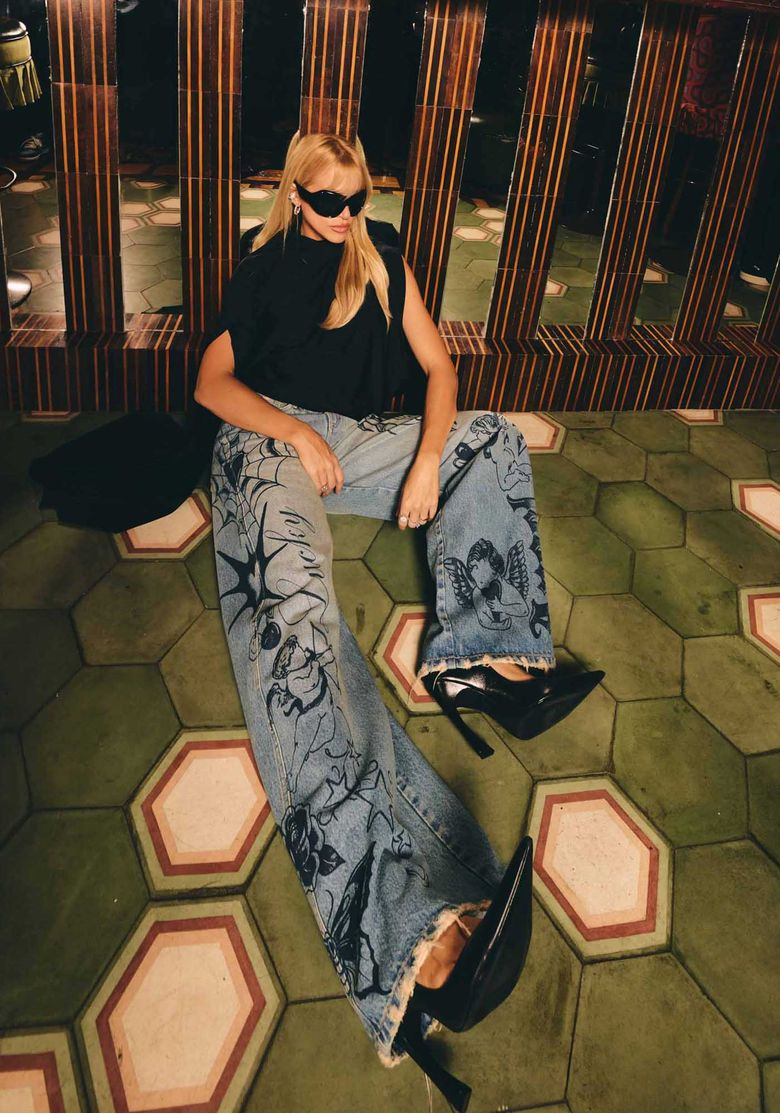 Editorial-de-moda-com-modelo-sentada-usando-calca-jeans-baggy-azul-estampada-e-blusa-preta-sofisticada