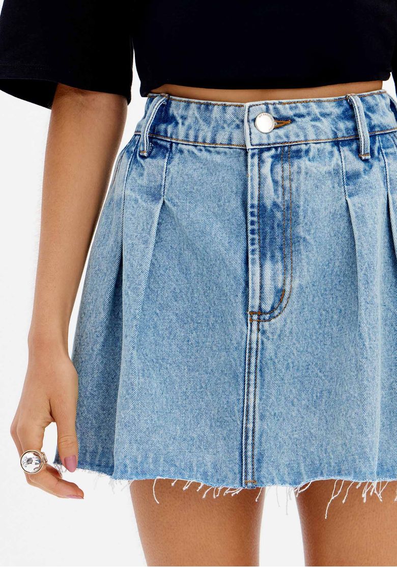 Detalhe da saia jeans curta com pregas, mostrando o cós com passantes e a barra desfiada.