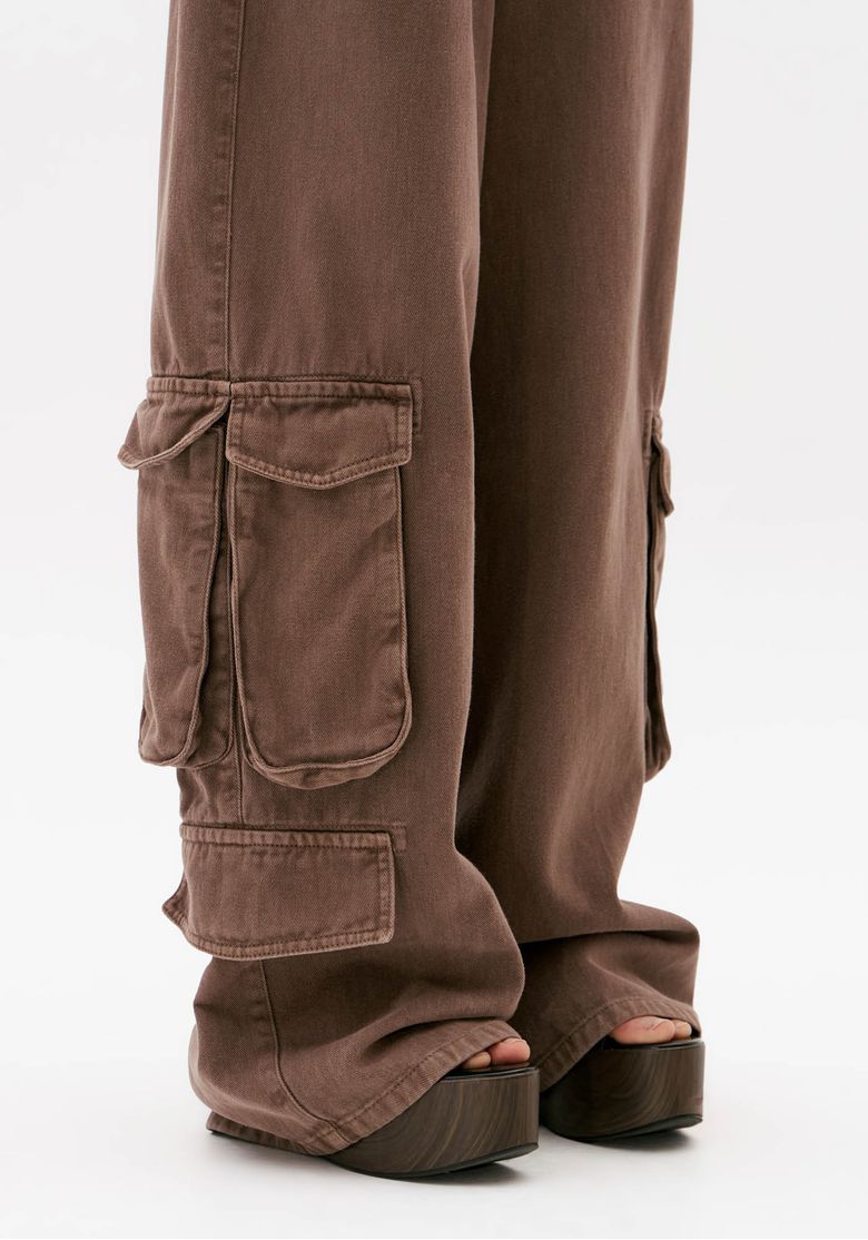 Close da calça cargo marrom feminina em sarja com bolso lateral utilitário de aba e barra longa ampla