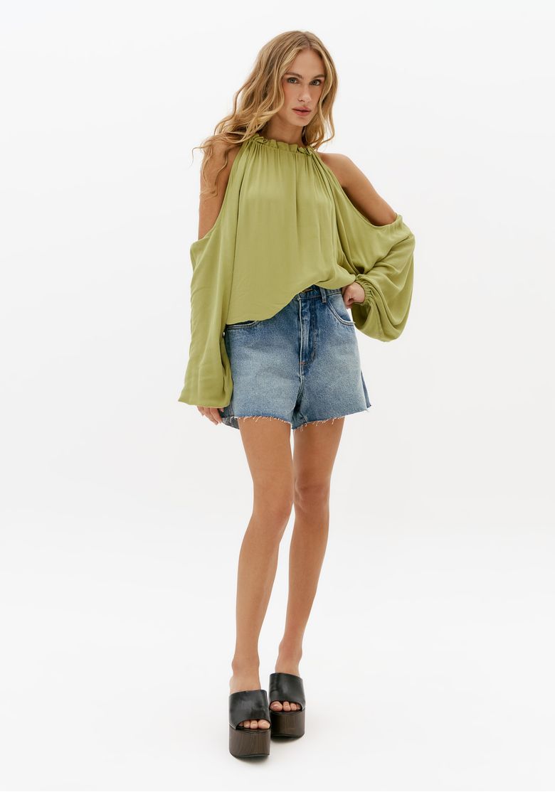 Modelo-usando-short-jeans-relaxed-azul-de-cintura-media-com-barra-desfiada-combinado-com-blusa-verde-fluida-e-tamanco-preto-plataforma