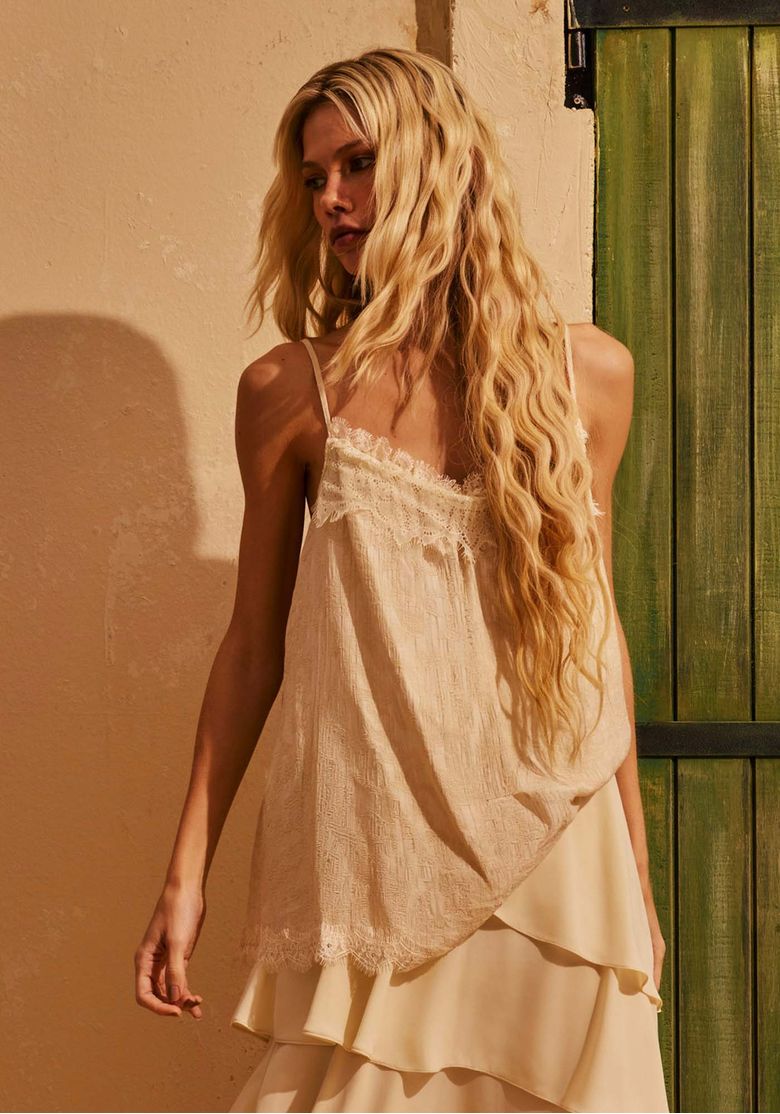 Blusa-feminina-de-alca-fina-off-white-com-renda-no-decote-e-na-barra-modelagem-ampla-e-caimento-fluido-em-foto-lifestyle