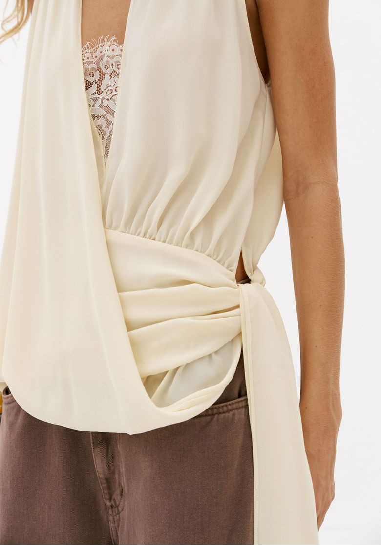 Close-da-blusa-transpassada-off-white-com-renda-no-decote-drapeado-lateral-e-faixa-alongada-assimetrica