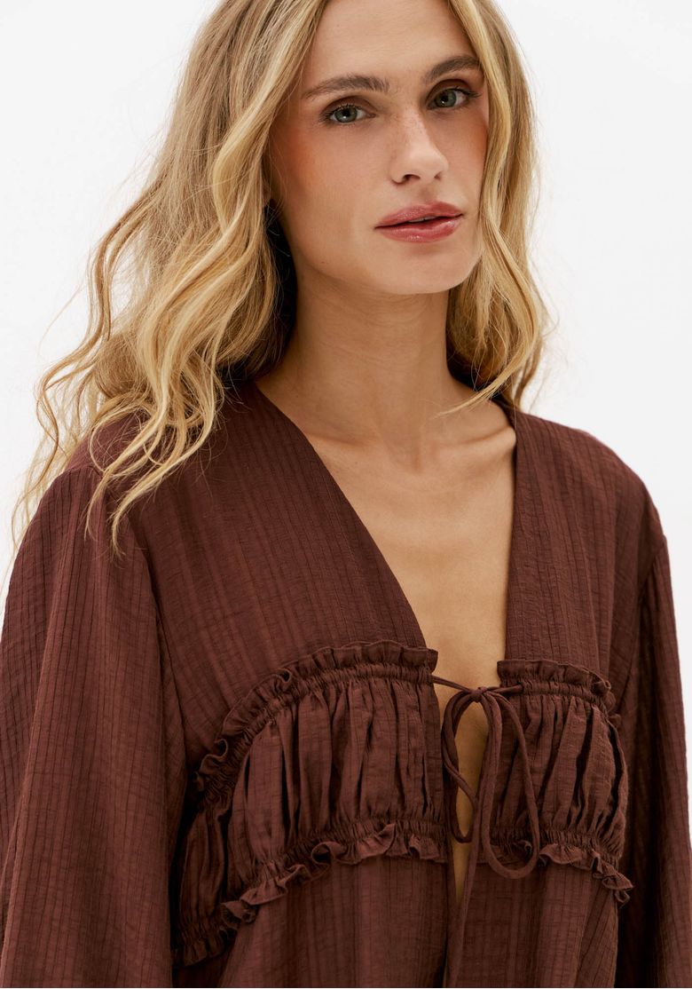 Close da blusa marrom com decote em V, babados na pala e amarração frontal