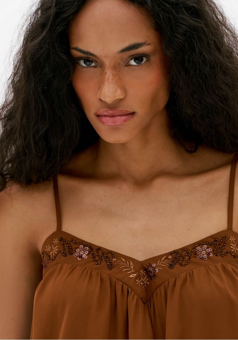 Close da blusa feminina marrom com alças finas e bordado aplicado no decote em V