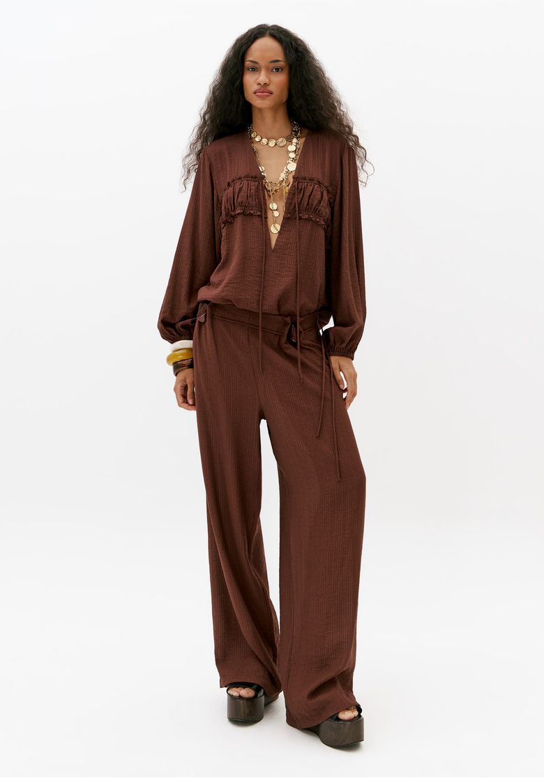 Modelo usando calça full length marrom feminina com pregas e aviamento lateral em look casual sofisticado com blusa fluida e sandália plataforma