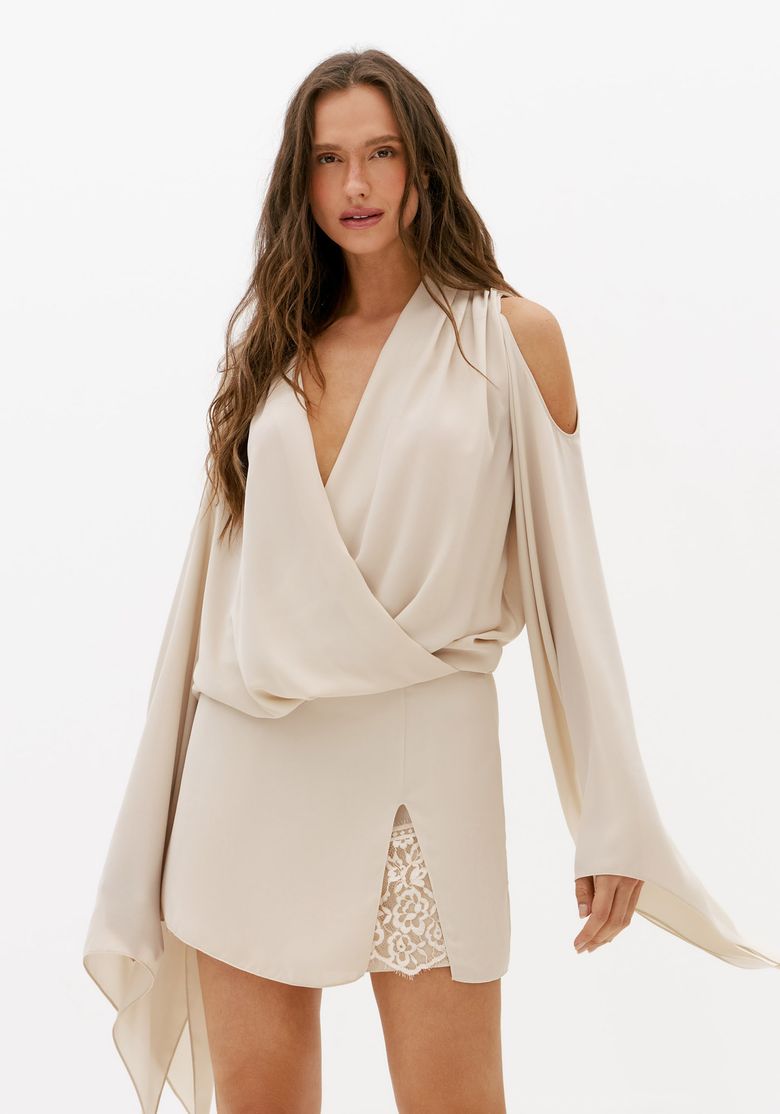 Modelo usando vestido curto off white com decote V, mangas longas fluidas e detalhe de renda frontal