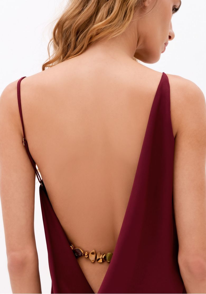 Close nas costas abertas do vestido bordô com degagê profundo, alça fina regulável e aplicação metálica