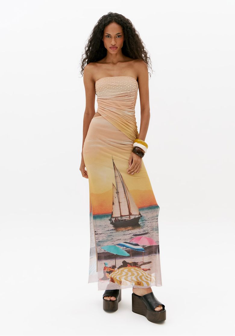 Vestido super midi de tule com brilho em foto de corpo inteiro, decote reto tomara que caia, recorte lateral e fenda frontal com estampa localizada de praia