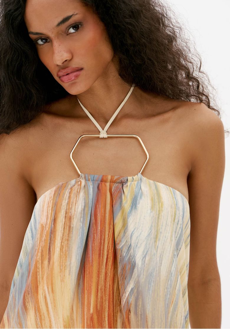 Close do busto de vestido frente única estampado com aro metálico no decote e tecido leve fluido