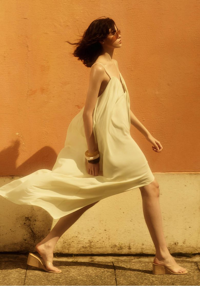 Vestido super midi off white em movimento com barra assimétrica, tecido leve e sandália de salto bloco em editorial de moda