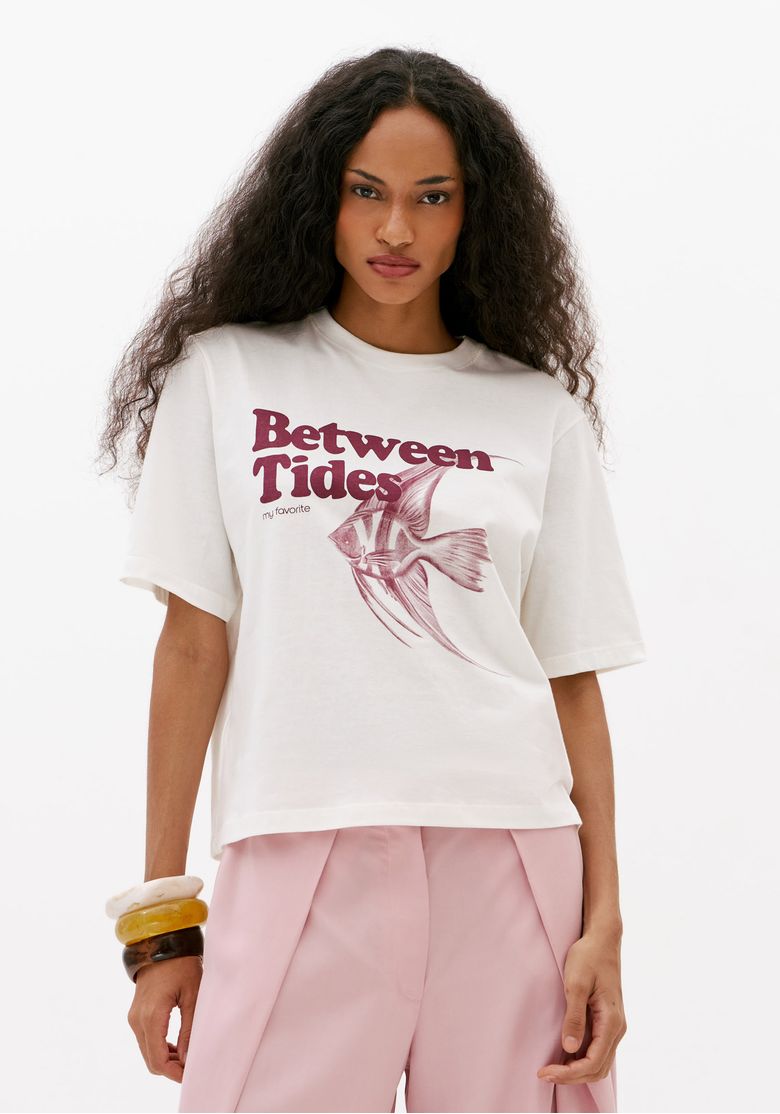 Modelo-com-camiseta-oversized-feminina-off-white-estampada-com-frase-Between-Tides-e-ilustracao-de-peixe-vista-frontal