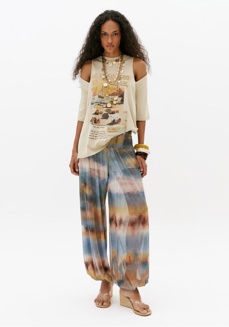 Look completo com t-shirt oversized open shoulder feminina off white e calça pantalona estampada multicolorida