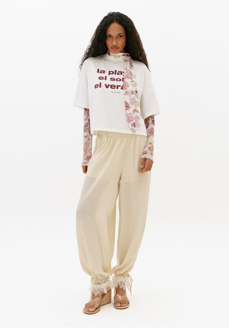 Vista-frontal-de-corpo-inteiro-de-camiseta-feminina-regular-off-white-com-mangas-curtas-estampa-frontal-e-lenco-combinada-com-calca-clara