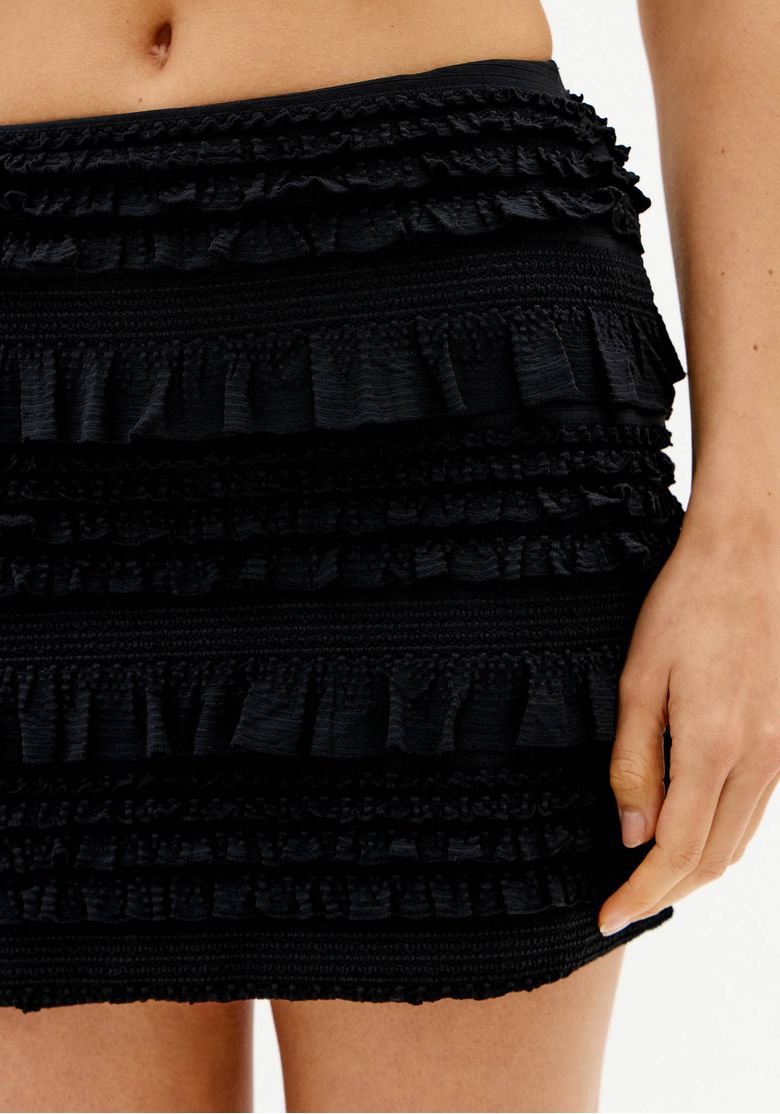 Close frontal da saia curta preta com textura em camadas de babados e cós elástico.