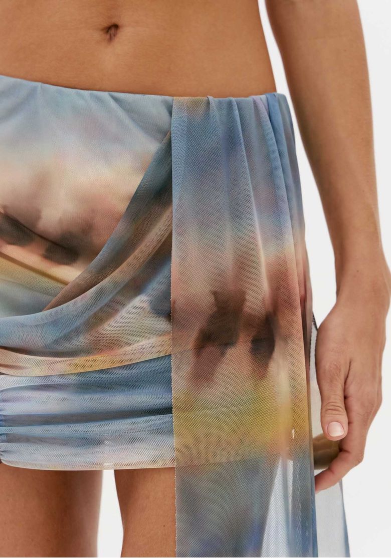 Detalhe da saia curta de tule estampada com sobreposição drapeada, estampa abstrata em azul e tons terrosos e tecido leve