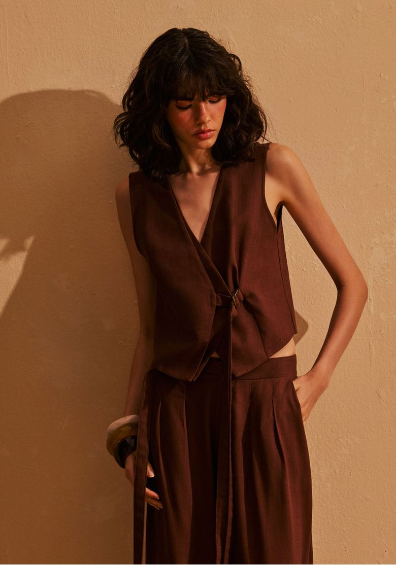 Modelo-usando-colete-feminino-marrom-de-alfaiataria-com-linho-e-amarracao-lateral-em-producao-elegante-de-tom-terroso