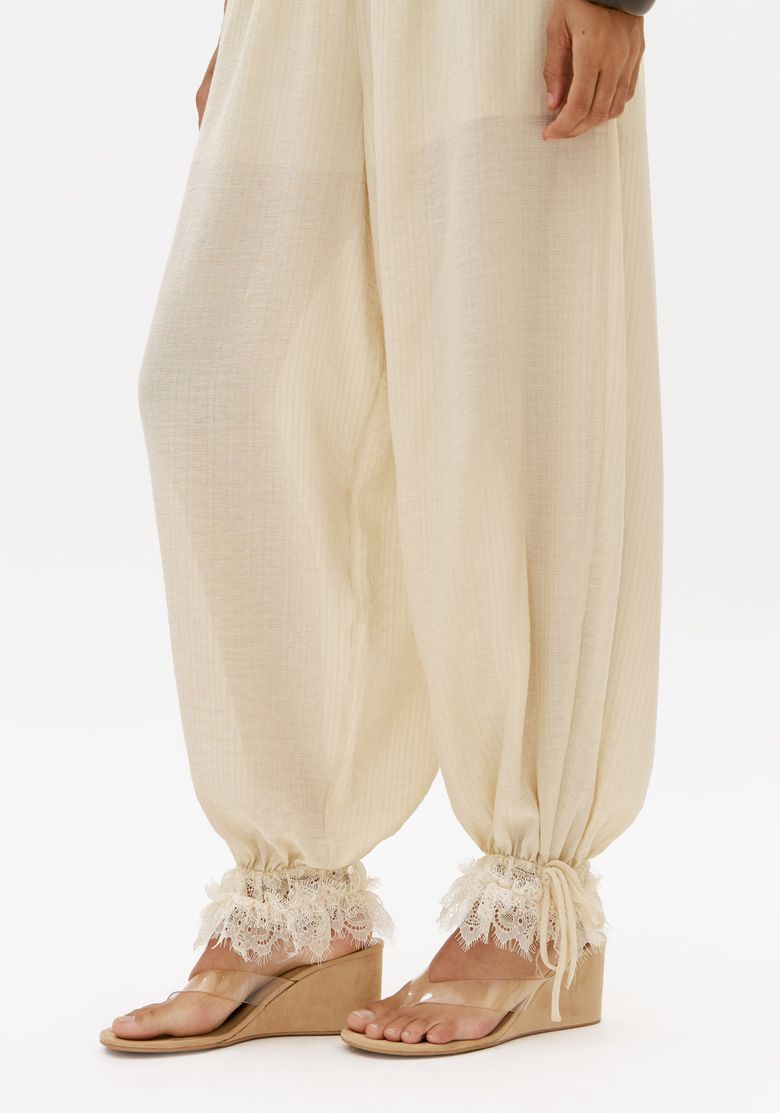 Detalhe-lateral-da-calca-aladim-feminina-off-white-com-volume-nas-pernas-e-acabamento-rendado-na-barra