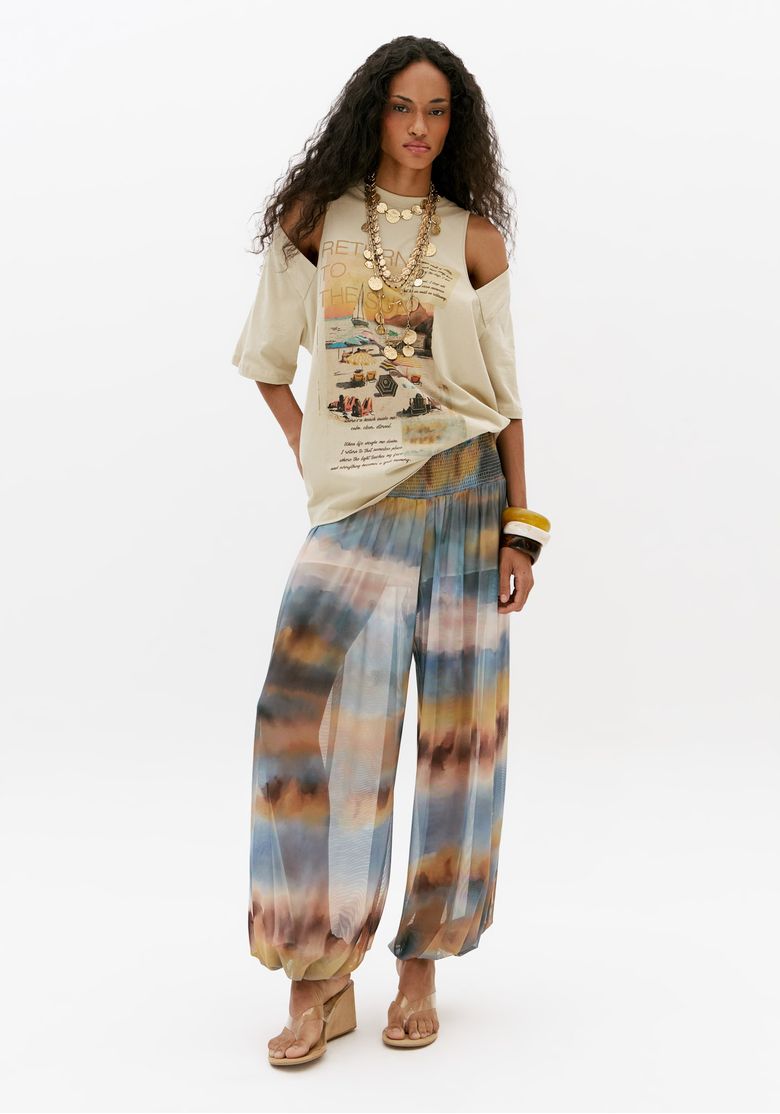 Modelo usando calça aladim feminina estampada em tule azul com pala de lastex, look leve de verão com caimento amplo e fluido