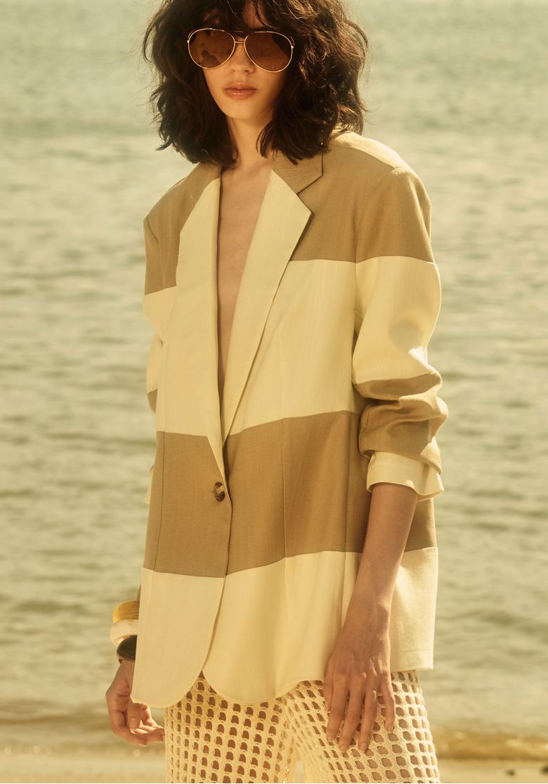 Blazer oversized bicolor feminino bege e off white com linho em foto lifestyle, peça de alfaiataria elegante com lapela clássica e fechamento por botão