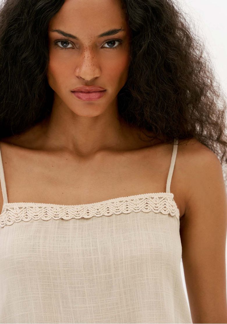 Close da blusa feminina off white de alça fina com detalhe de crochê aplicado no decote e textura leve de linho