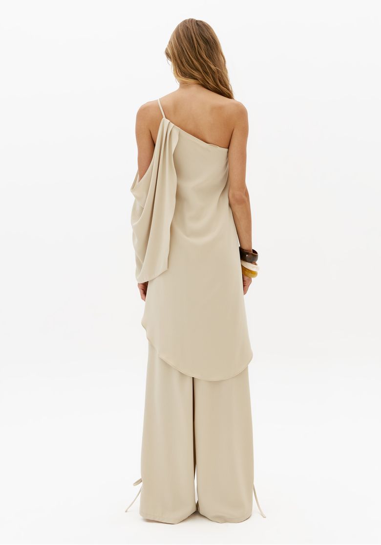 Vista traseira do look feminino com blusa alongada ombro único off white e calça pantalona em estúdio